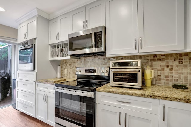 kitchen with backsplash, light stone counters, stainless steel appliances, white cabinets, and light hardwood / wood-style floors