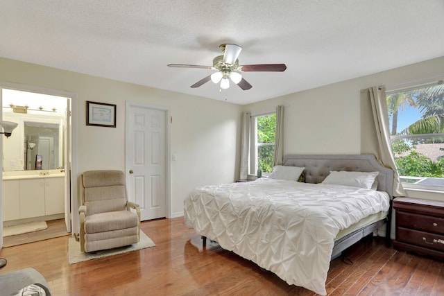 bedroom featuring ceiling fan, ensuite bathroom, wood-type flooring, and a textured ceiling