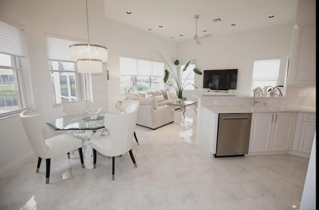 dining space featuring ceiling fan with notable chandelier, sink, and a high ceiling