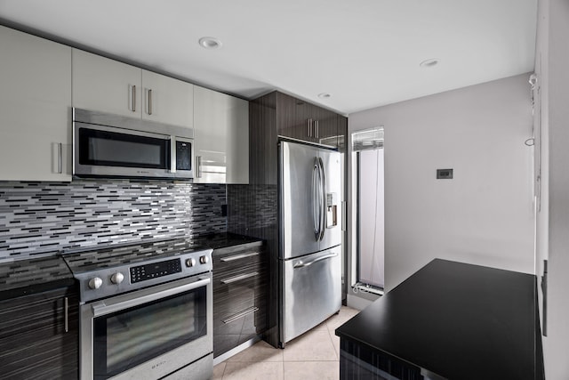 kitchen with tasteful backsplash, light tile patterned flooring, dark brown cabinets, white cabinets, and appliances with stainless steel finishes