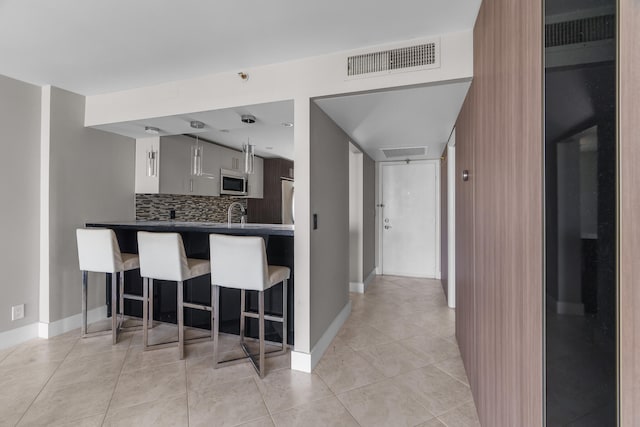 kitchen with decorative backsplash, kitchen peninsula, a breakfast bar, light tile patterned floors, and white cabinets