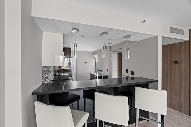 kitchen with hanging light fixtures, tasteful backsplash, a kitchen breakfast bar, kitchen peninsula, and light tile patterned floors