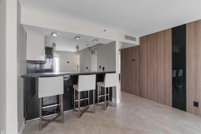 kitchen featuring a breakfast bar area, tasteful backsplash, light tile patterned floors, and decorative light fixtures