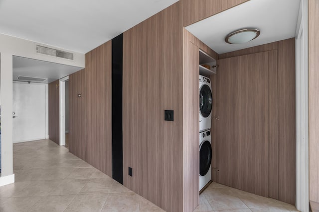 laundry room with wood walls, light tile patterned floors, and stacked washer and clothes dryer