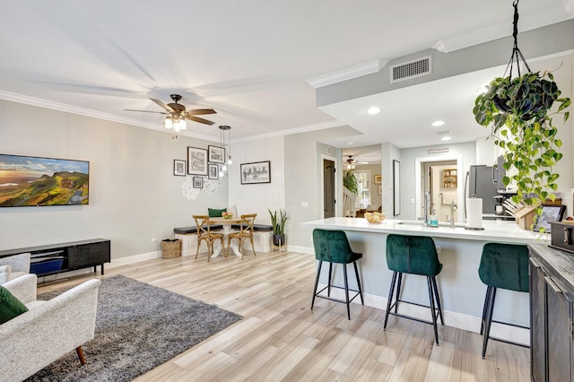 kitchen featuring pendant lighting, a kitchen breakfast bar, crown molding, and light hardwood / wood-style flooring