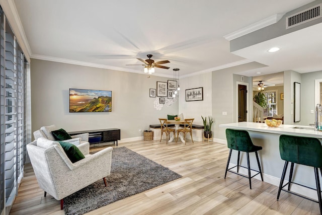 living room featuring ceiling fan, ornamental molding, and light hardwood / wood-style flooring