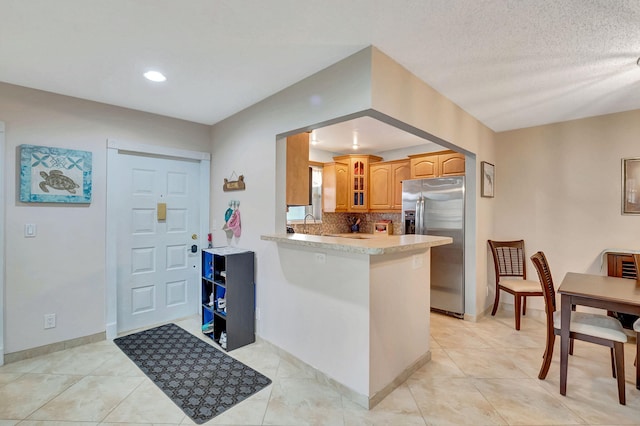 kitchen with kitchen peninsula, tasteful backsplash, a textured ceiling, light tile patterned floors, and stainless steel fridge with ice dispenser