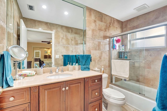 full bathroom with vanity, toilet, tile walls, ceiling fan, and bath / shower combo with glass door