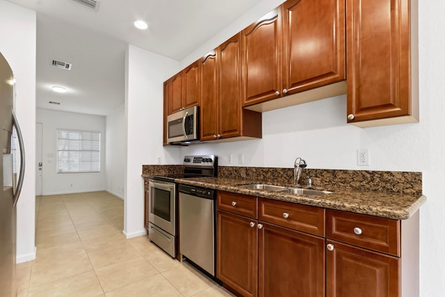 kitchen featuring dark stone countertops, sink, light tile patterned flooring, and stainless steel appliances