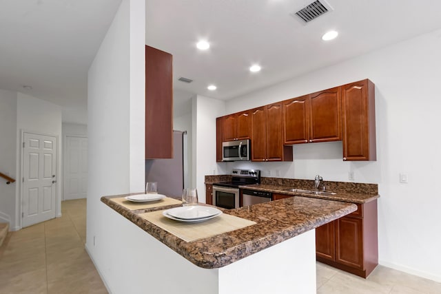 kitchen with kitchen peninsula, stainless steel appliances, sink, dark stone countertops, and light tile patterned flooring