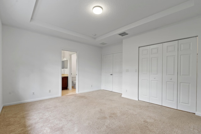 unfurnished bedroom featuring a raised ceiling, ensuite bath, light colored carpet, and a textured ceiling