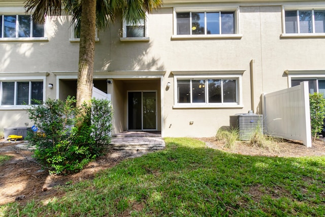 rear view of property featuring central air condition unit and a lawn