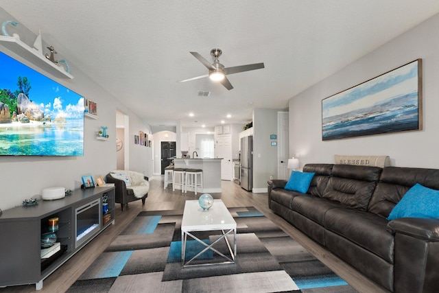 living room with a textured ceiling, ceiling fan, and dark hardwood / wood-style floors