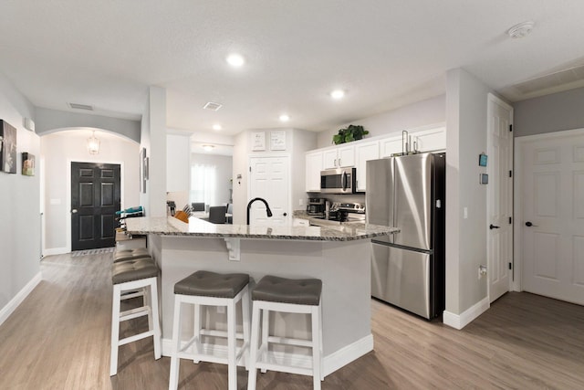 kitchen with a kitchen bar, white cabinetry, light wood-type flooring, and appliances with stainless steel finishes