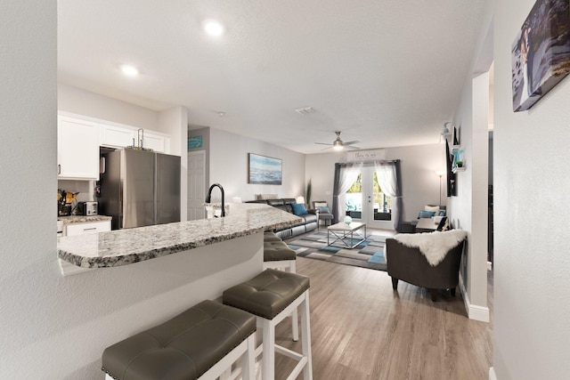 kitchen with light stone countertops, stainless steel fridge, french doors, white cabinets, and light hardwood / wood-style floors