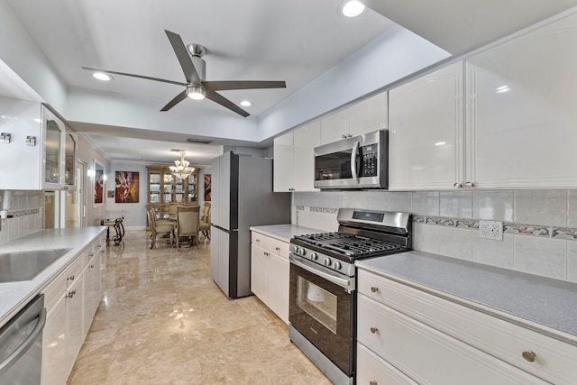 kitchen featuring backsplash, ceiling fan with notable chandelier, stainless steel appliances, sink, and white cabinetry