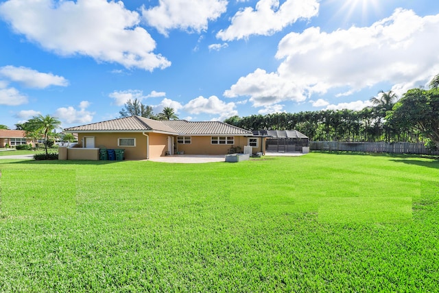 rear view of house featuring a yard, glass enclosure, and a patio