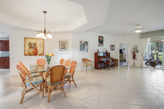 tiled dining room with a raised ceiling and ceiling fan with notable chandelier