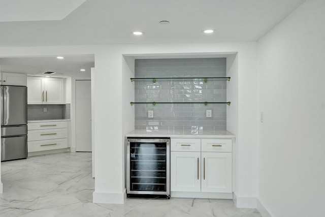 bar featuring stainless steel refrigerator, wine cooler, decorative backsplash, and white cabinetry