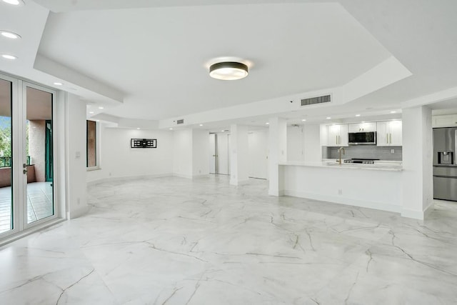 unfurnished living room featuring a raised ceiling and sink