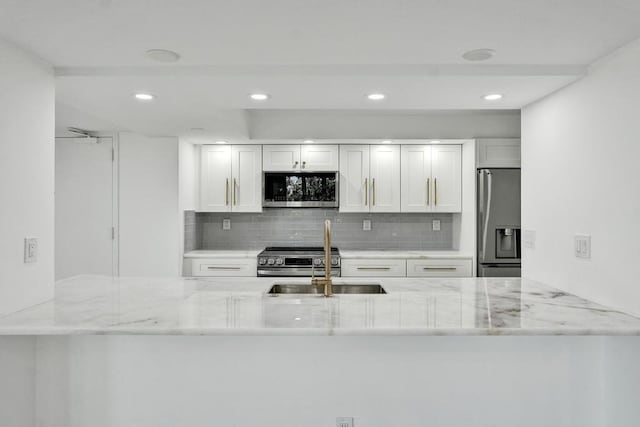 kitchen with backsplash, white cabinetry, light stone countertops, and appliances with stainless steel finishes