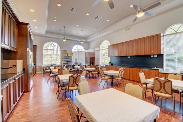 dining room with ceiling fan, a raised ceiling, and light hardwood / wood-style flooring