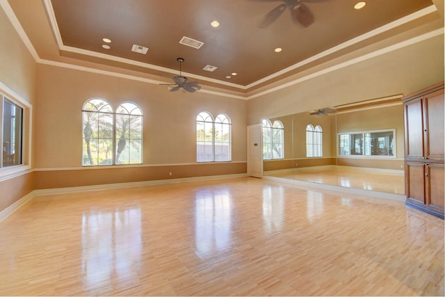 unfurnished room with a towering ceiling, a raised ceiling, ceiling fan, crown molding, and light hardwood / wood-style flooring