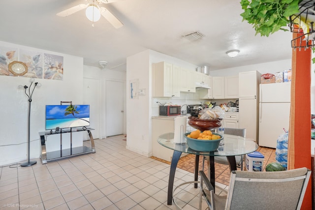 kitchen with ceiling fan, white fridge, white cabinetry, and light tile patterned floors