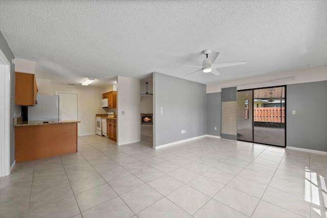 unfurnished living room with ceiling fan, light tile patterned floors, and a textured ceiling