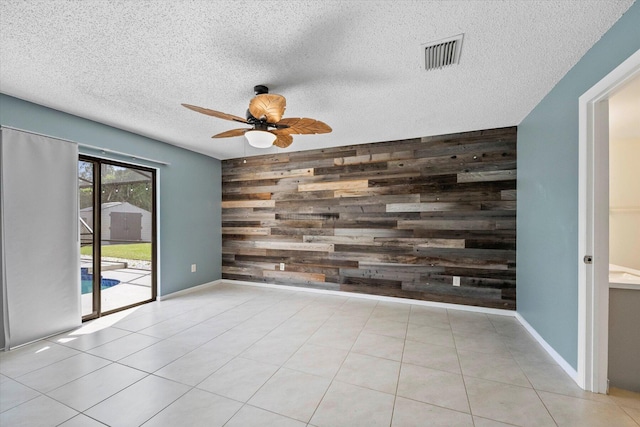 tiled empty room with wooden walls, ceiling fan, and a textured ceiling