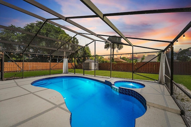 pool at dusk featuring an in ground hot tub, a lanai, a patio area, a shed, and a lawn