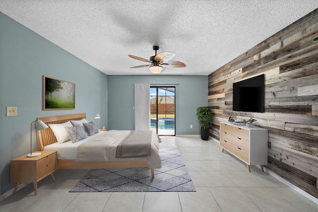 tiled bedroom featuring access to outside, wood walls, ceiling fan, and a textured ceiling