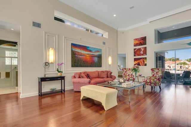 living room with hardwood / wood-style floors, a towering ceiling, and ornamental molding