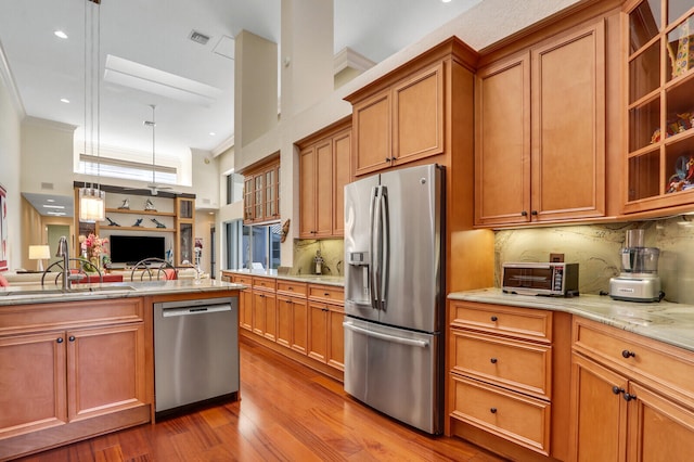 kitchen with appliances with stainless steel finishes, light wood-type flooring, tasteful backsplash, crown molding, and pendant lighting