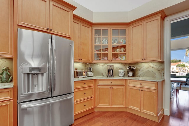 kitchen with light stone countertops, stainless steel refrigerator with ice dispenser, light hardwood / wood-style floors, and tasteful backsplash