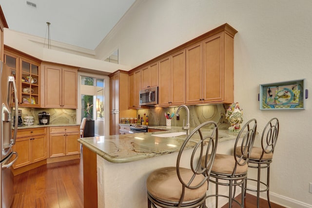 kitchen featuring stainless steel appliances, tasteful backsplash, dark hardwood / wood-style flooring, kitchen peninsula, and a breakfast bar area