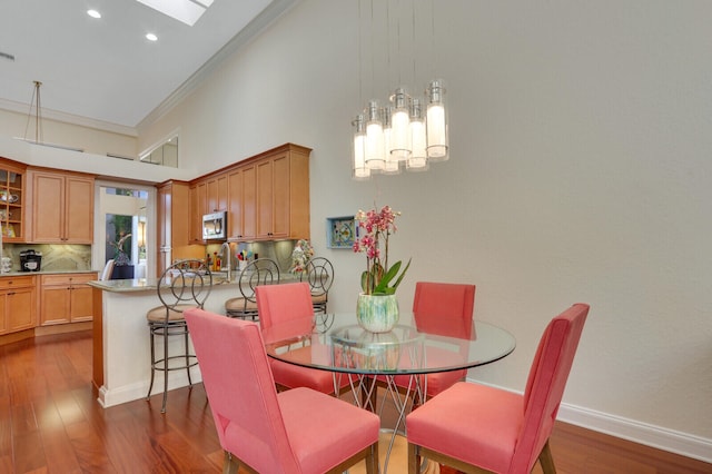 dining space featuring a skylight, crown molding, a towering ceiling, and dark wood-type flooring