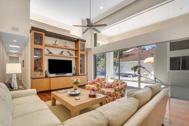 living room with a high ceiling, light wood-type flooring, ceiling fan, and ornamental molding