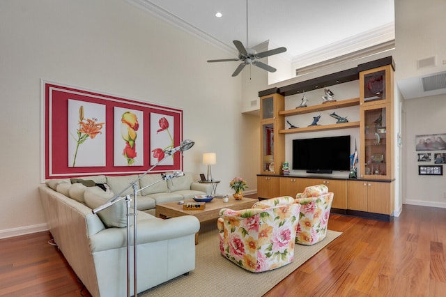 living room with a high ceiling, hardwood / wood-style flooring, ceiling fan, and crown molding