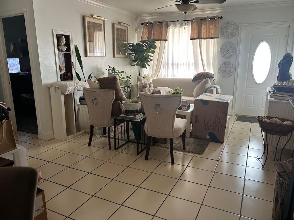 tiled dining area with ceiling fan and crown molding