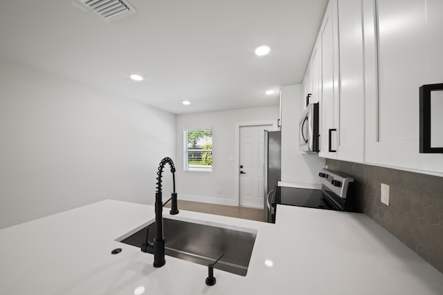 kitchen with decorative backsplash, white cabinetry, sink, and appliances with stainless steel finishes