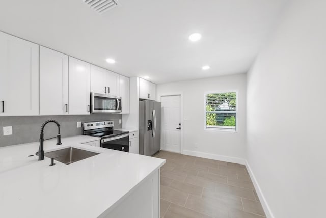 kitchen with sink, light tile patterned floors, tasteful backsplash, white cabinets, and appliances with stainless steel finishes