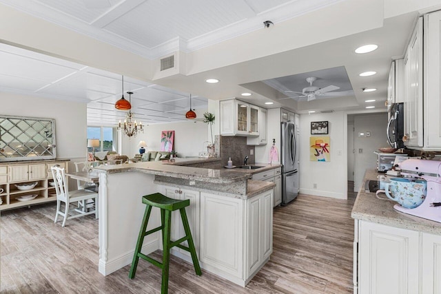 kitchen featuring pendant lighting, stainless steel appliances, light stone counters, white cabinets, and kitchen peninsula