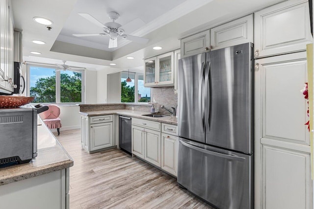 kitchen featuring sink, appliances with stainless steel finishes, a tray ceiling, a healthy amount of sunlight, and light wood-type flooring