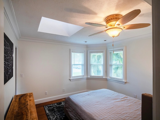 bedroom with a skylight, ornamental molding, a textured ceiling, ceiling fan, and dark wood-type flooring