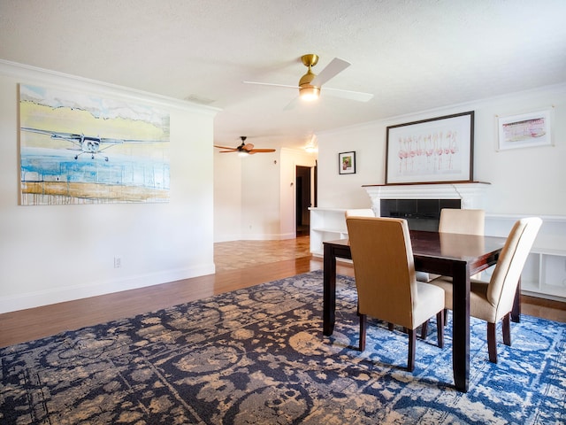 dining space with hardwood / wood-style flooring, ceiling fan, crown molding, and a fireplace