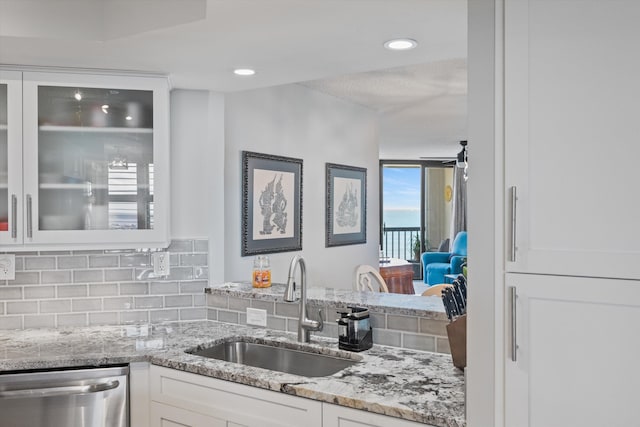 kitchen with decorative backsplash, light stone countertops, stainless steel dishwasher, sink, and white cabinets