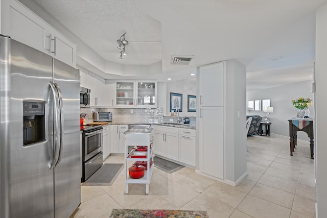 kitchen with stainless steel appliances, light tile patterned floors, a textured ceiling, decorative backsplash, and white cabinets