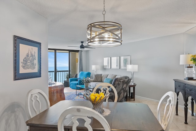 tiled dining room with a textured ceiling, ceiling fan with notable chandelier, a water view, and a wall of windows