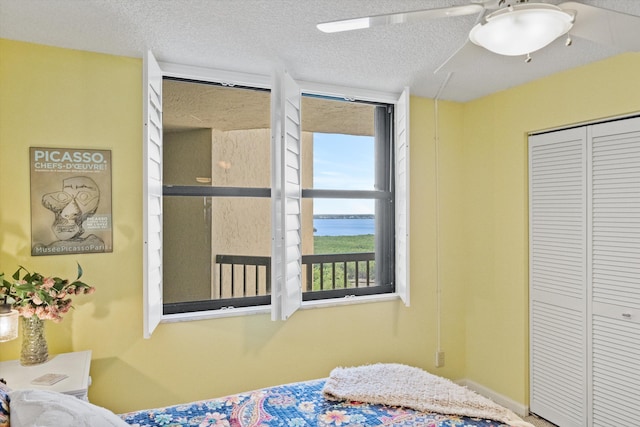 bedroom with ceiling fan, a water view, a textured ceiling, and a closet